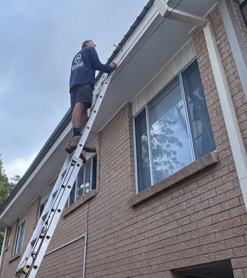 Roofer on a ladder assessing a damaged roof